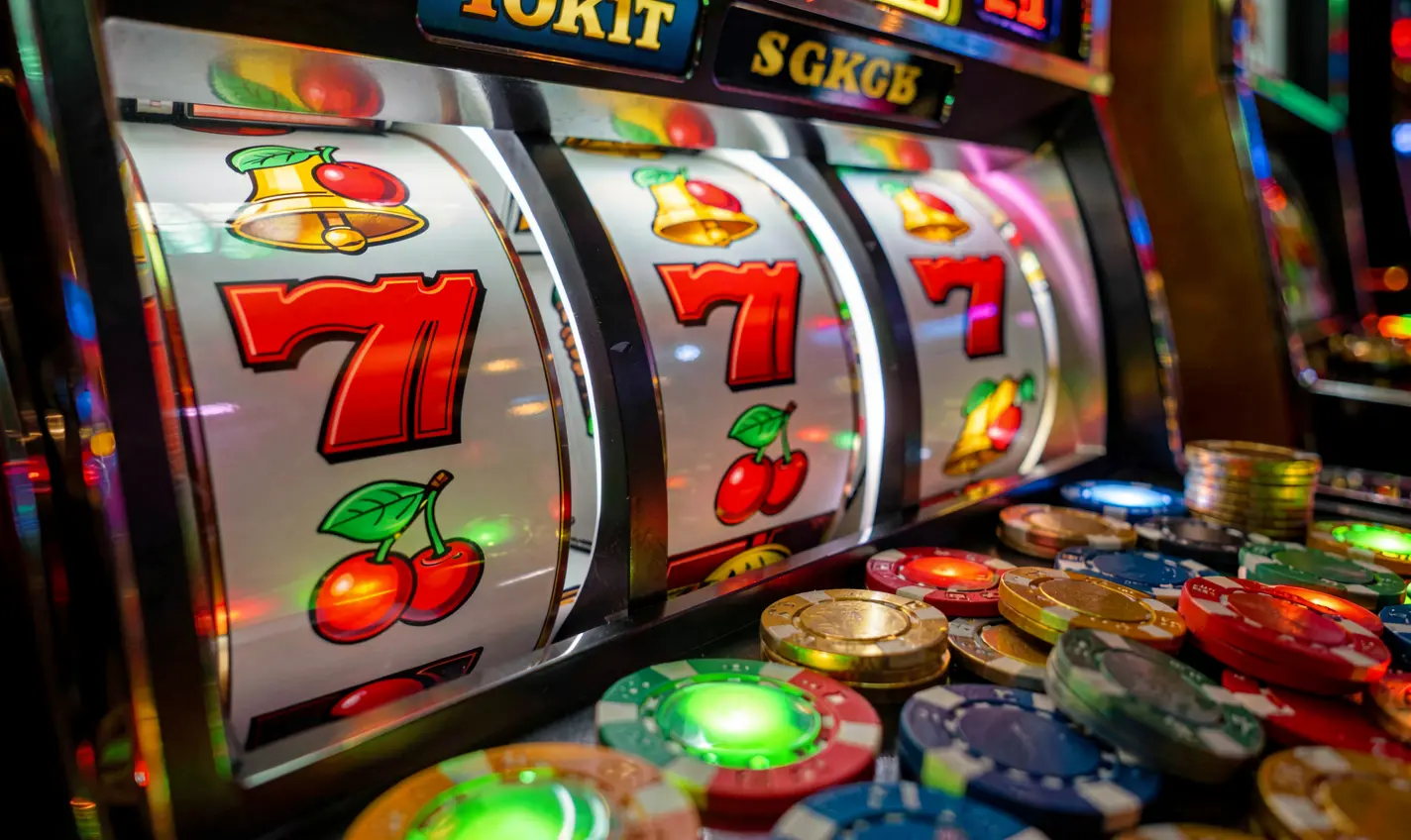 Close-up view of vibrant slot reels with red sevens, cherries, and golden bells surrounded by casino chips representing premium slot gaming at 26OK